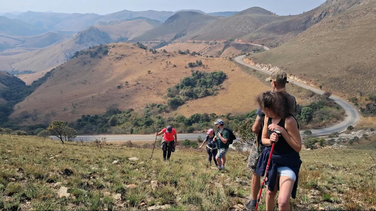 Hikers on a grassy slope of the Makhonjwa Mountains beside the winding geotrail pass